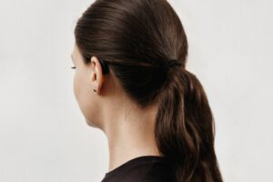 woman with long brown hair in a ponytail wearing Fortell prescription AI hearing aid, seen behind the ear